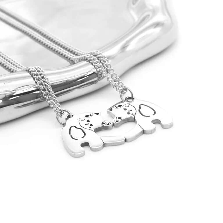 Des Colliers pour couple au design de chat formant un cœur sur un support blanc